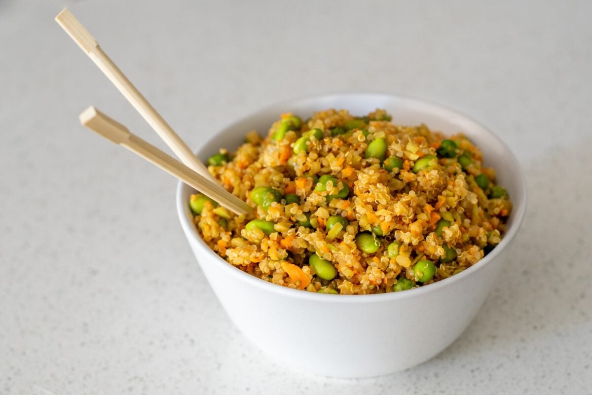 A white bowl with quinoa fried rice in it and a set of wooden chopsticks sticking out.
