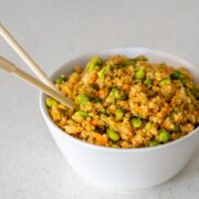 A white bowl with quinoa fried rice in it and a set of wooden chopsticks sticking out.