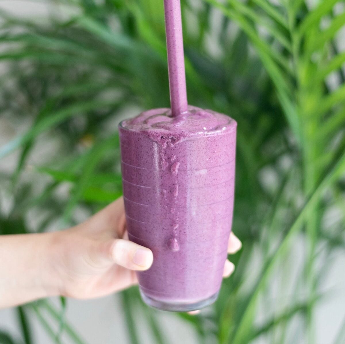 A purple smoothie in a clear cup with a straw.