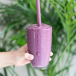 A purple smoothie in a clear cup with a straw.
