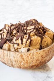 A brown bowl filled with multiple scoops of chickpea vegan peanut butter ice cream topped with melted drizzled chocolate.
