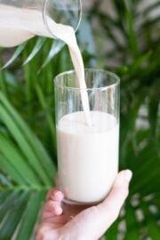 A glass filled with milk and a pitcher pouring more milk into the glass.