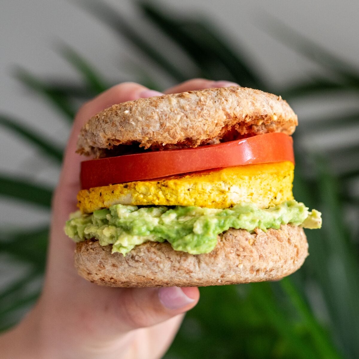 A vegan breakfast sandwich being held by a white hand.