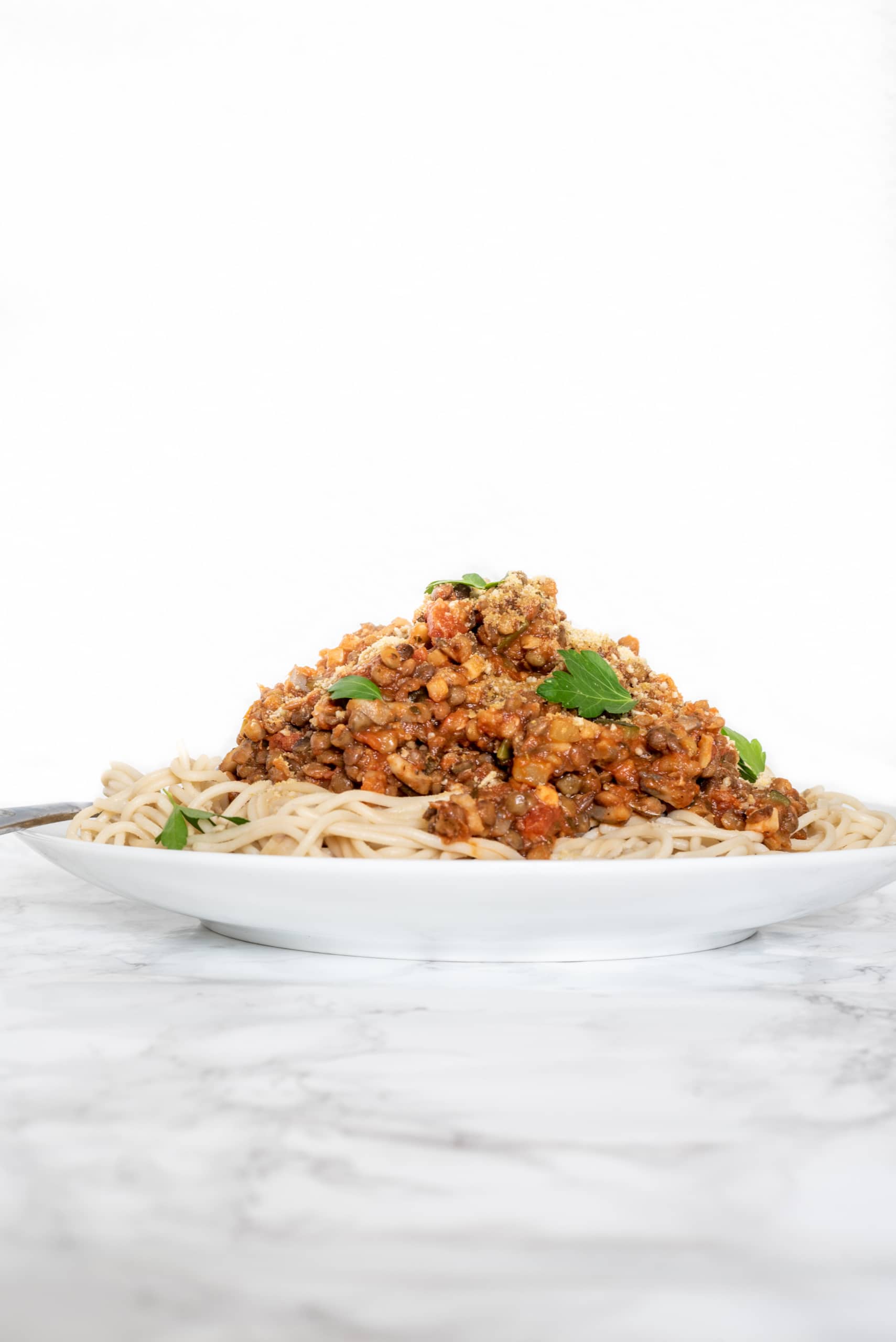 A plate stacked with spaghetti noodles with lentil bolognese on top garnished with parsley.