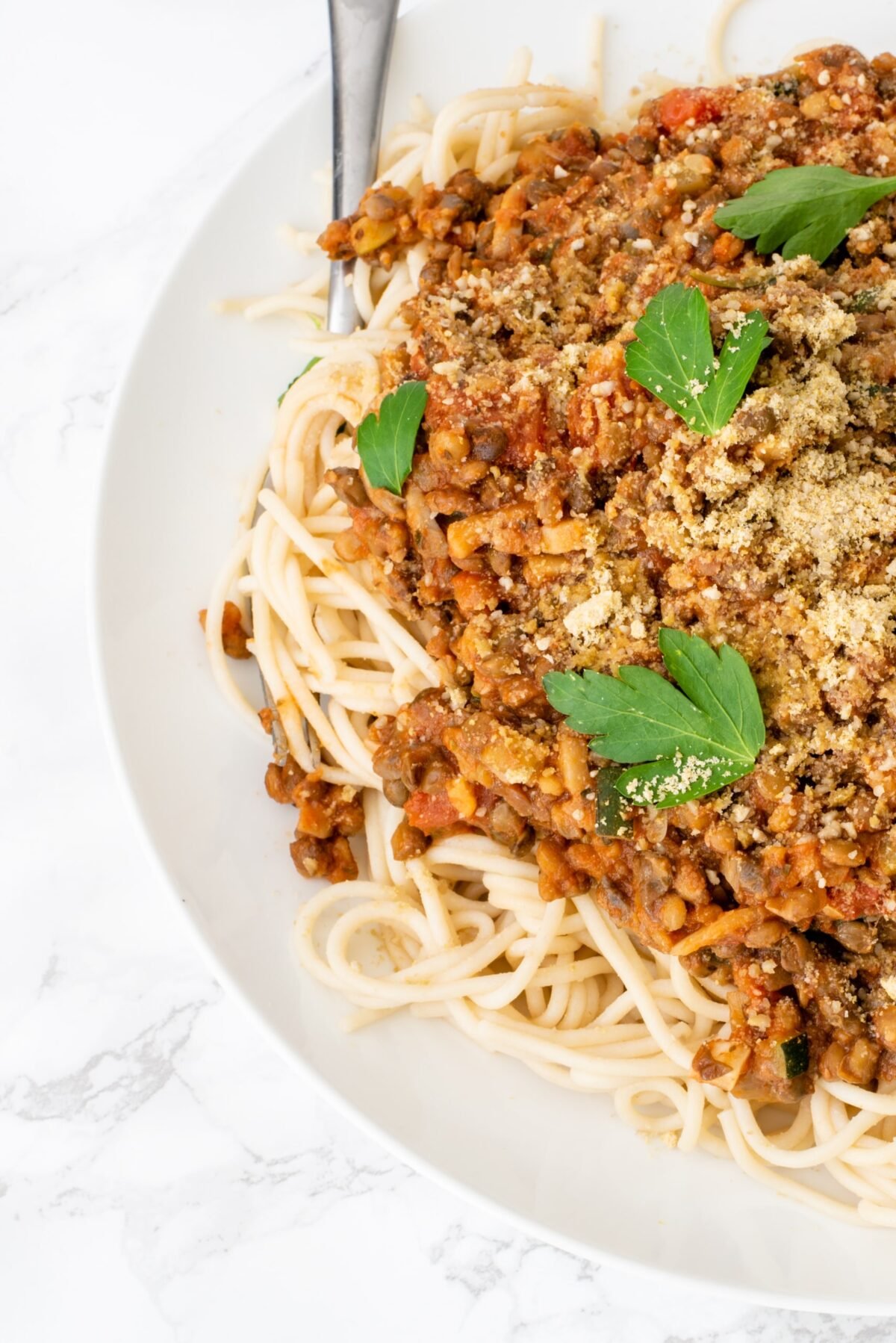 Half of a plate with spaghetti noodles and lentil bolognese on top garnished with parsley.