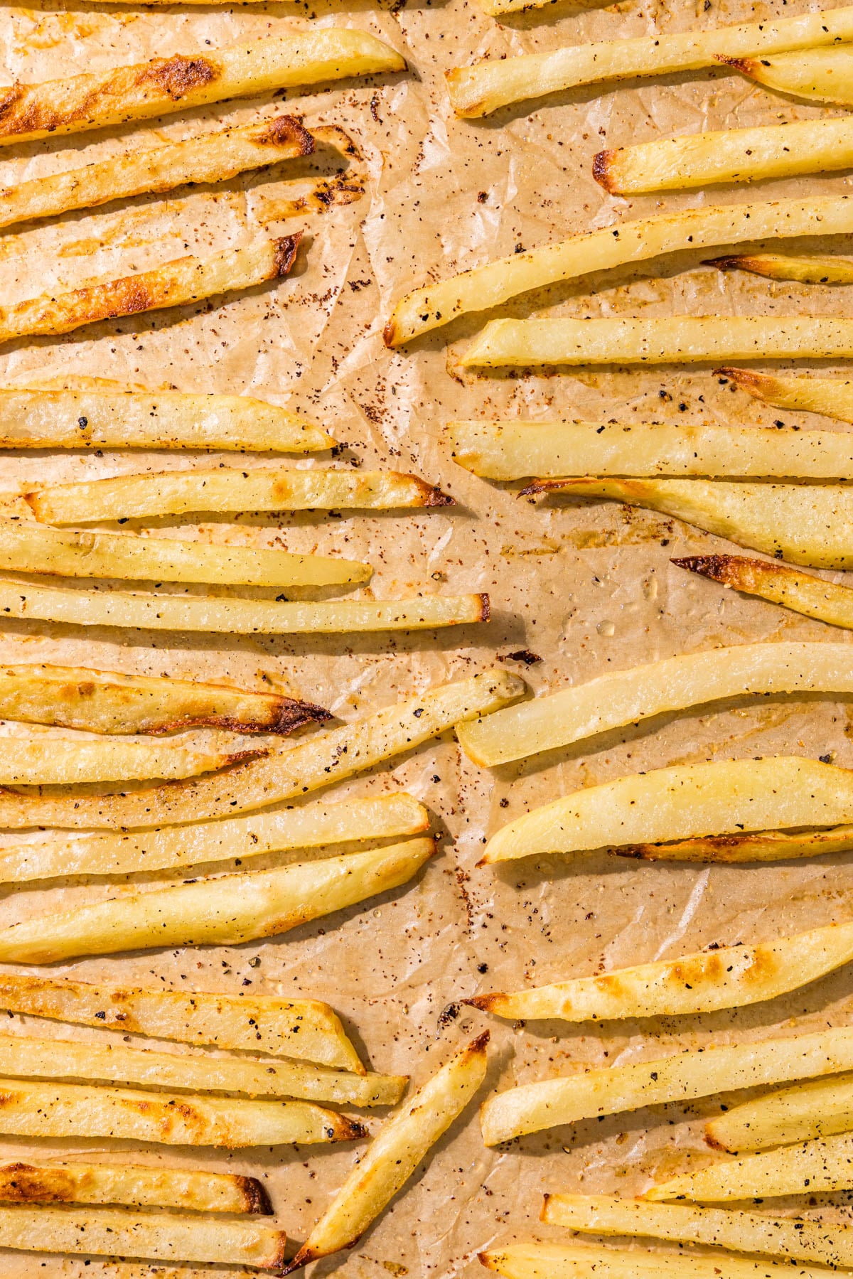 A pan lined with parchment paper topped with baked crispy fries.