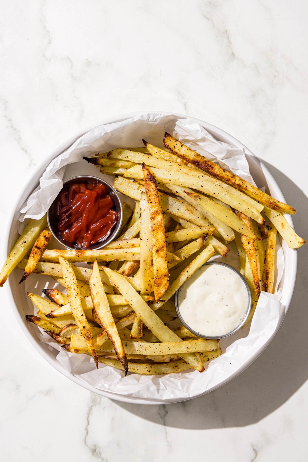 A bowl of fries with two containers of dipping sauces ranch and ketchup.