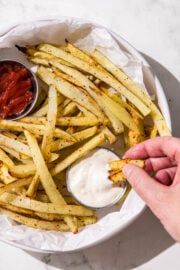 A white bowl filled with french fries and two silver containers of ketchup and ranch.