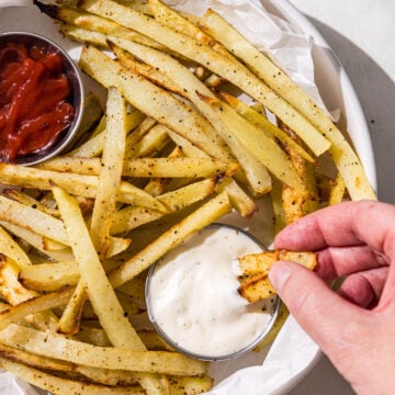 A white bowl filled with french fries and two silver containers of ketchup and ranch.