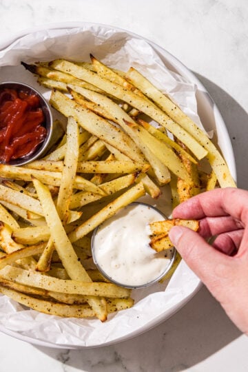 A white bowl filled with french fries and two silver containers of ketchup and ranch.