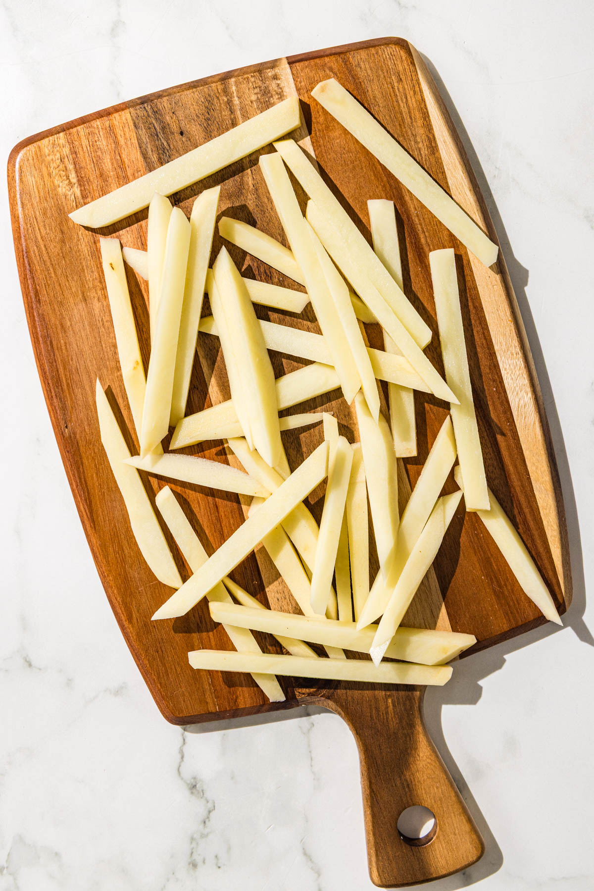 A brown wooden cutting board with sliced potatoes on it.