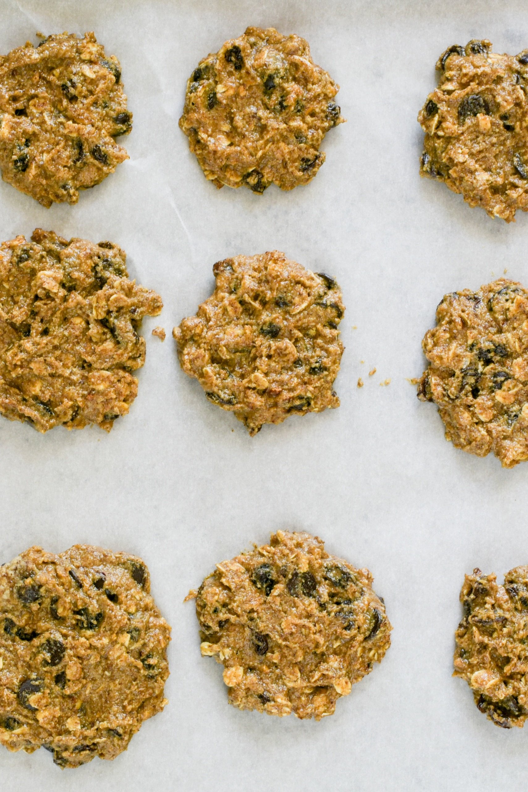 A baking pan lined with parchment with 9 oatmeal raisin cookies scooped out onto it ready to be baked.
