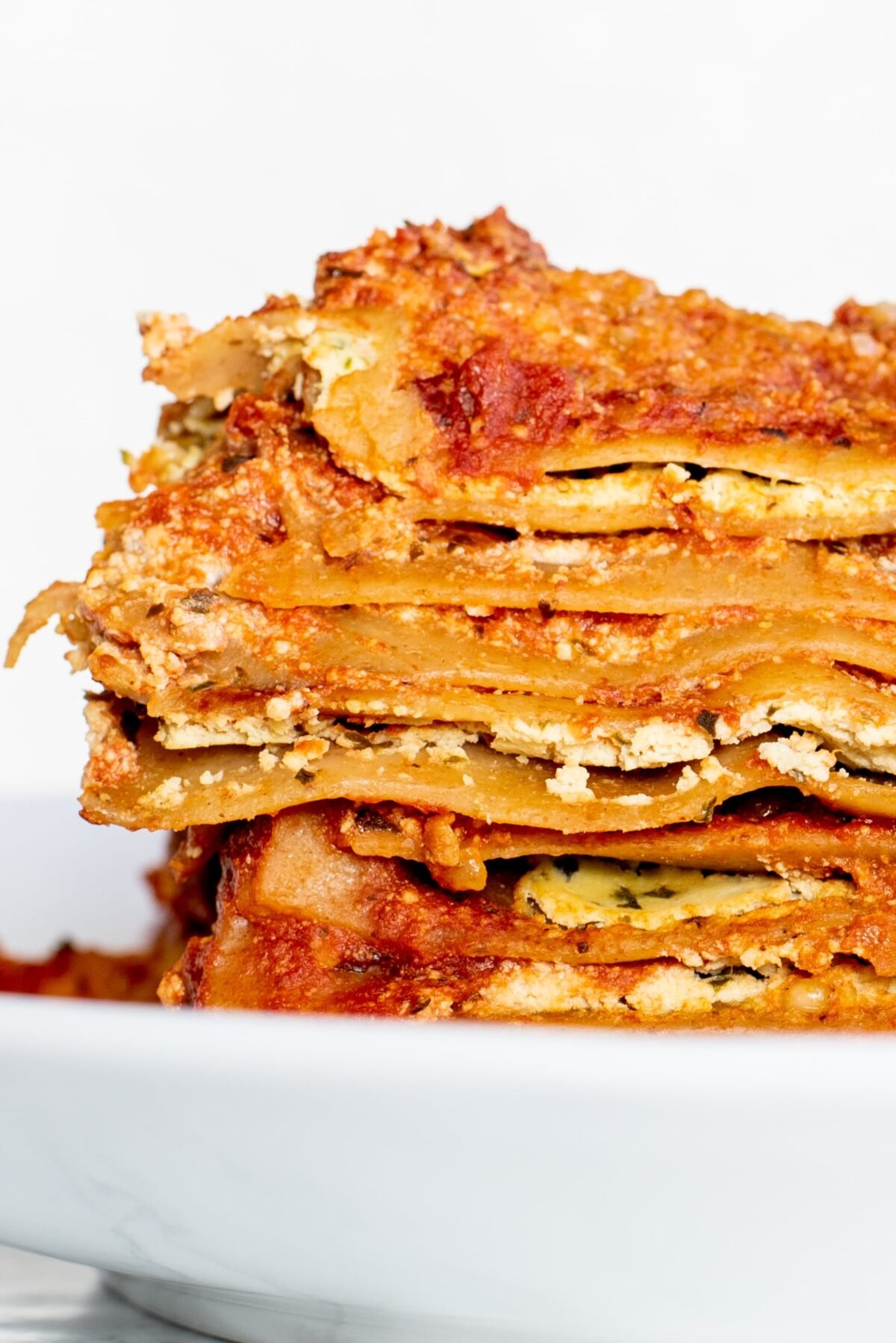 A close up of a layered slice of lasagna on a white plate.