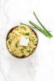 A bowl of mashed potatoes with a square of butter and fresh chives on top.