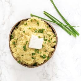 A bowl of mashed potatoes with a square of butter and fresh chives on top.