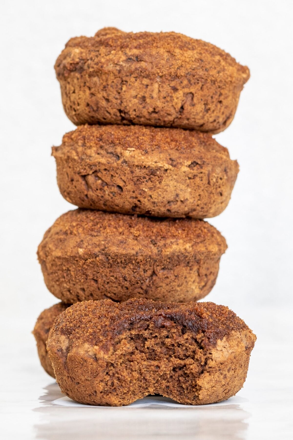 A stack of four cinnamon sugar donuts and a fifth one in front on the counter with a bite taken out of it.
