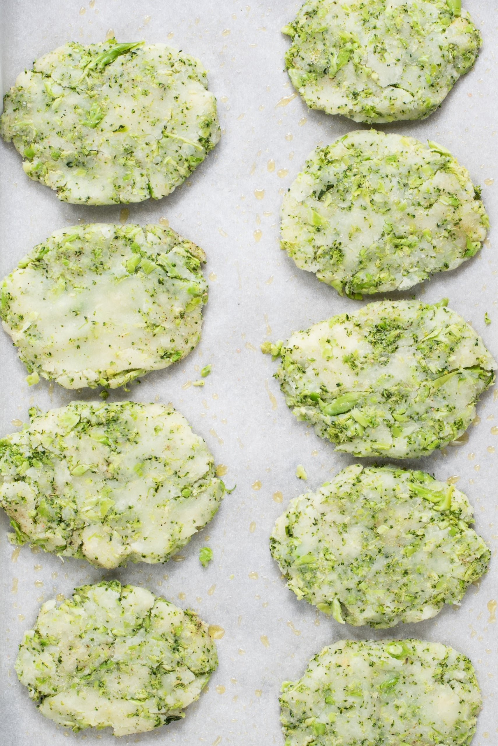 Nine broccoli potato hashbrown patties on a tray ready to be baked.