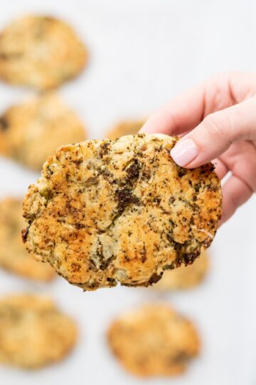 A white hand holding a broccoli potato hashbrown.