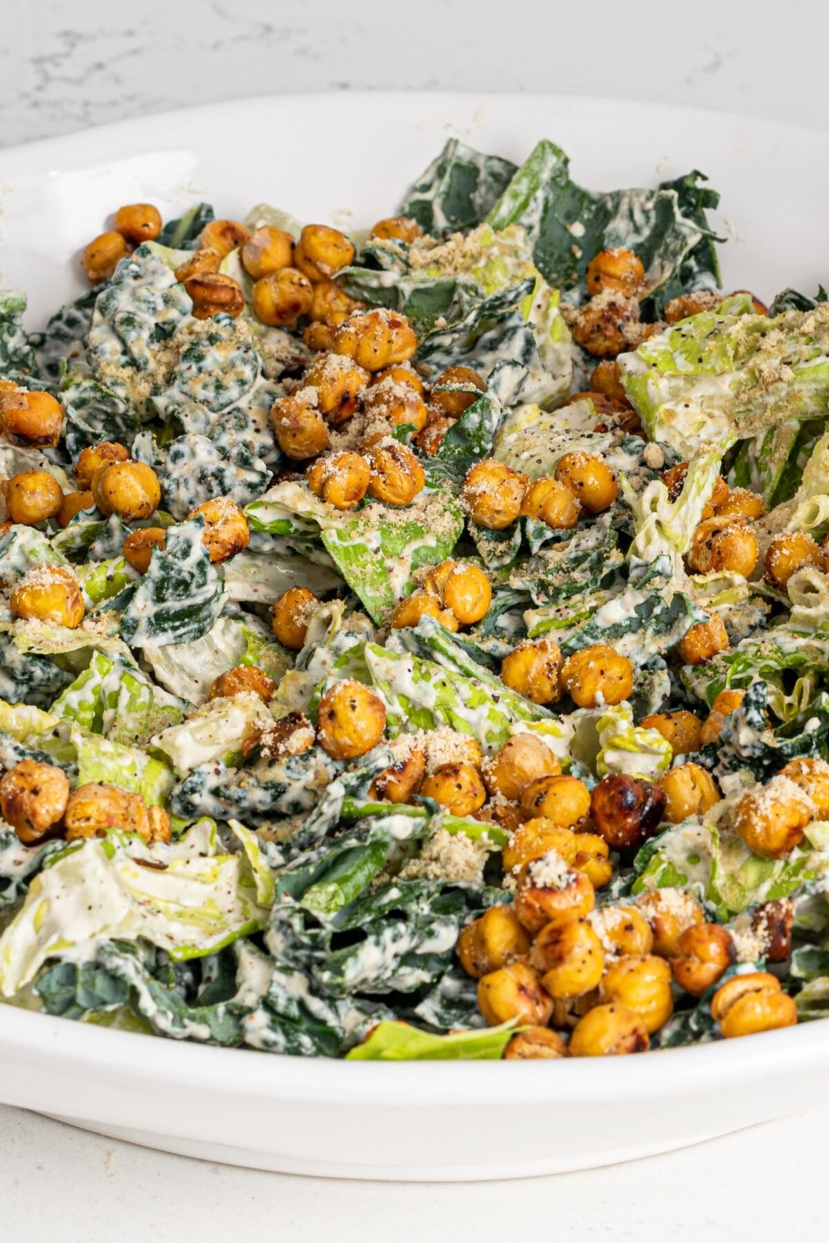 A white bowl filled with romaine, kale, creamy dressing and crispy chickpeas on top.