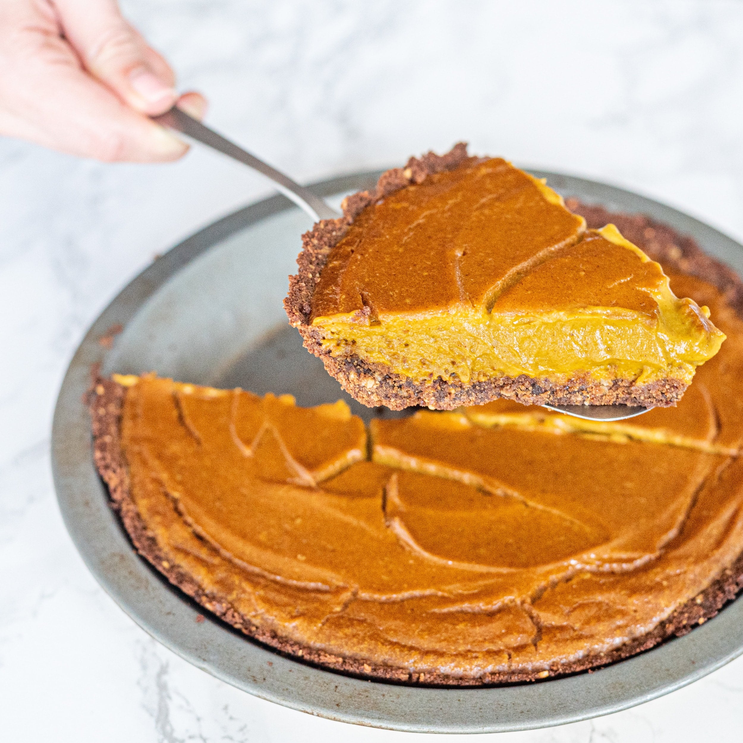 A pumpkin pie with a slice cut out of it and a spatula holding a slice of pie.