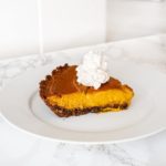 A slice of pumpkin pie topped with whipped cream on a white plate.