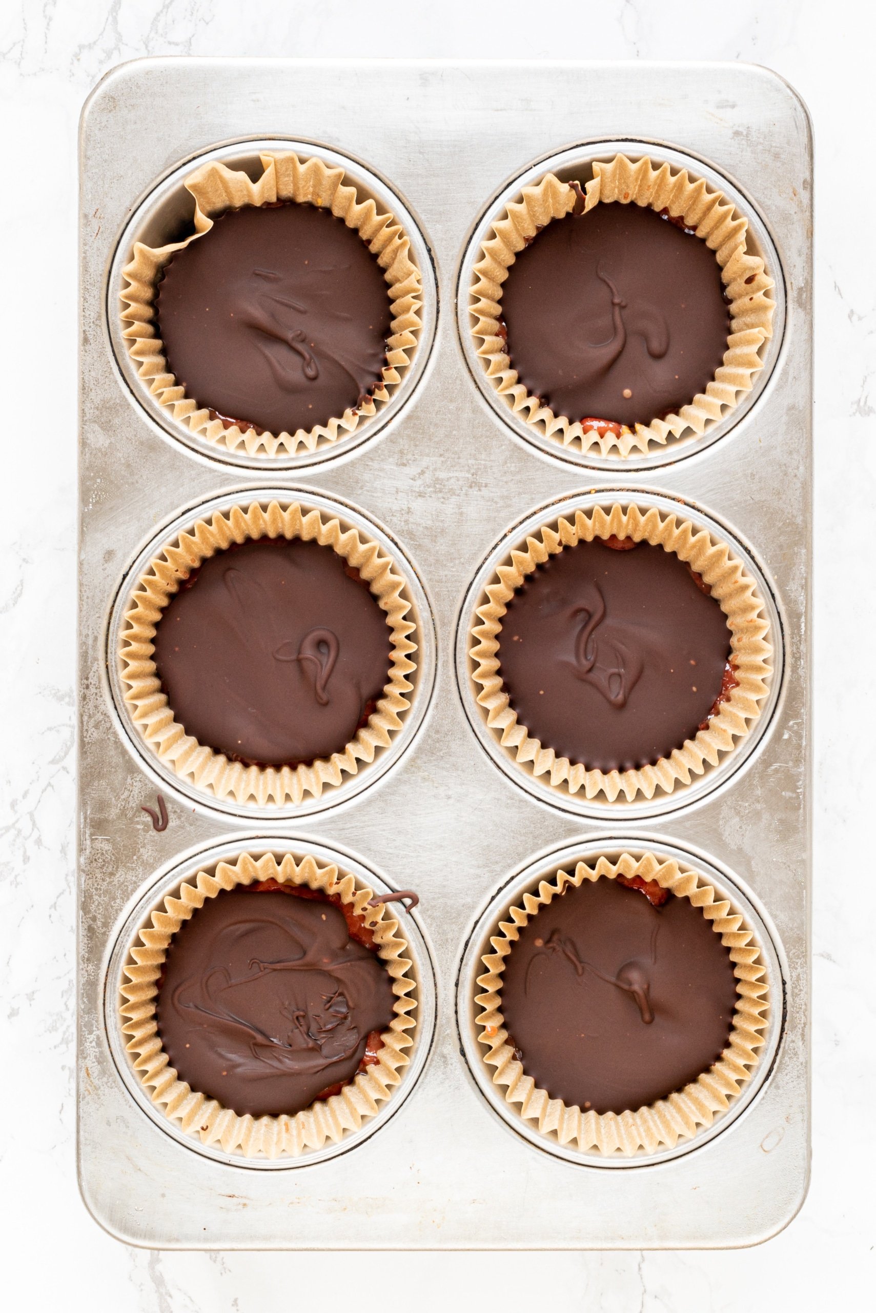 A muffin tin lined with 6 muffin liners filled with chocolate.