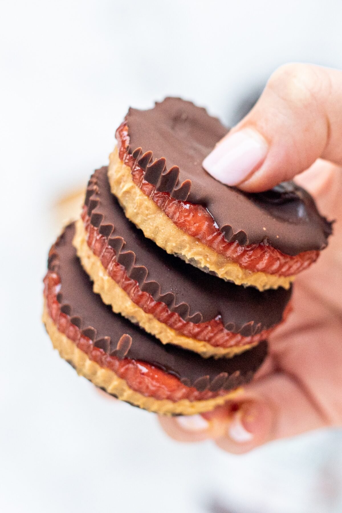 Three peanut butter and jelly cups stacked on top of each other being held by a white hand.