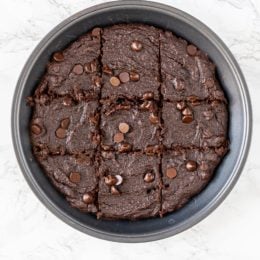 A circular pan filled with brownies cut into 9 pieces with chocolate chips on top.