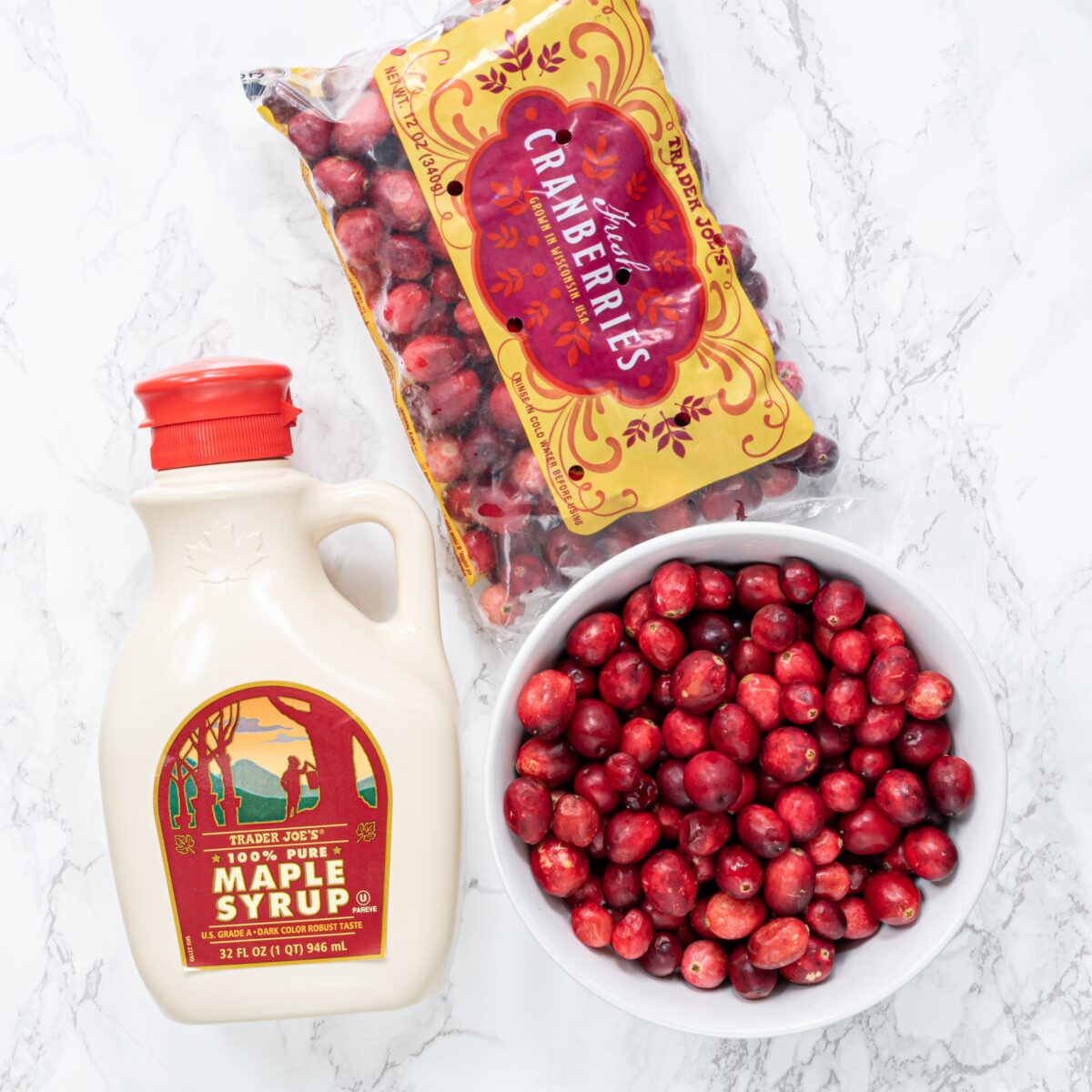 A jar of maple syrup, a bag of cranberries and a bowl of fresh cranberries.