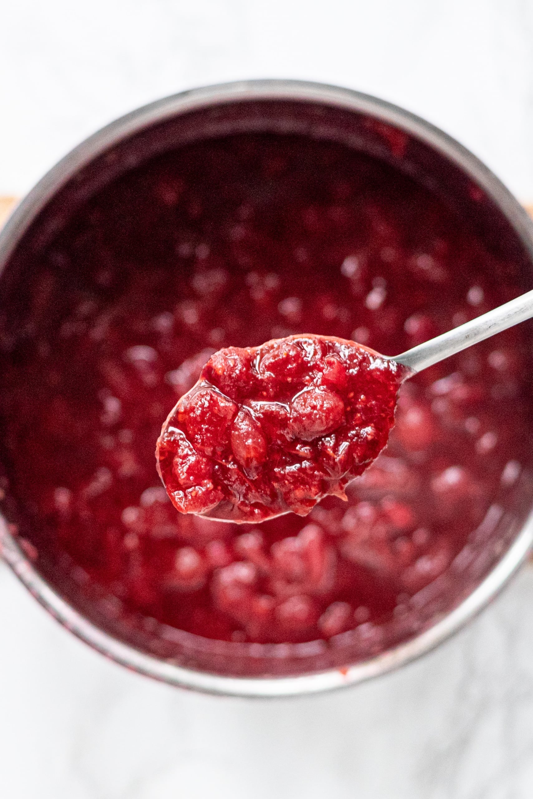 A silver pot of cranberry sauce and a silver spoon holding a scoop of cranberry sauce.