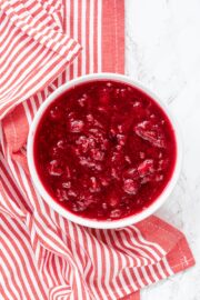 A white bowl of cranberry sauce with a white and red striped towel beside the bowl.
