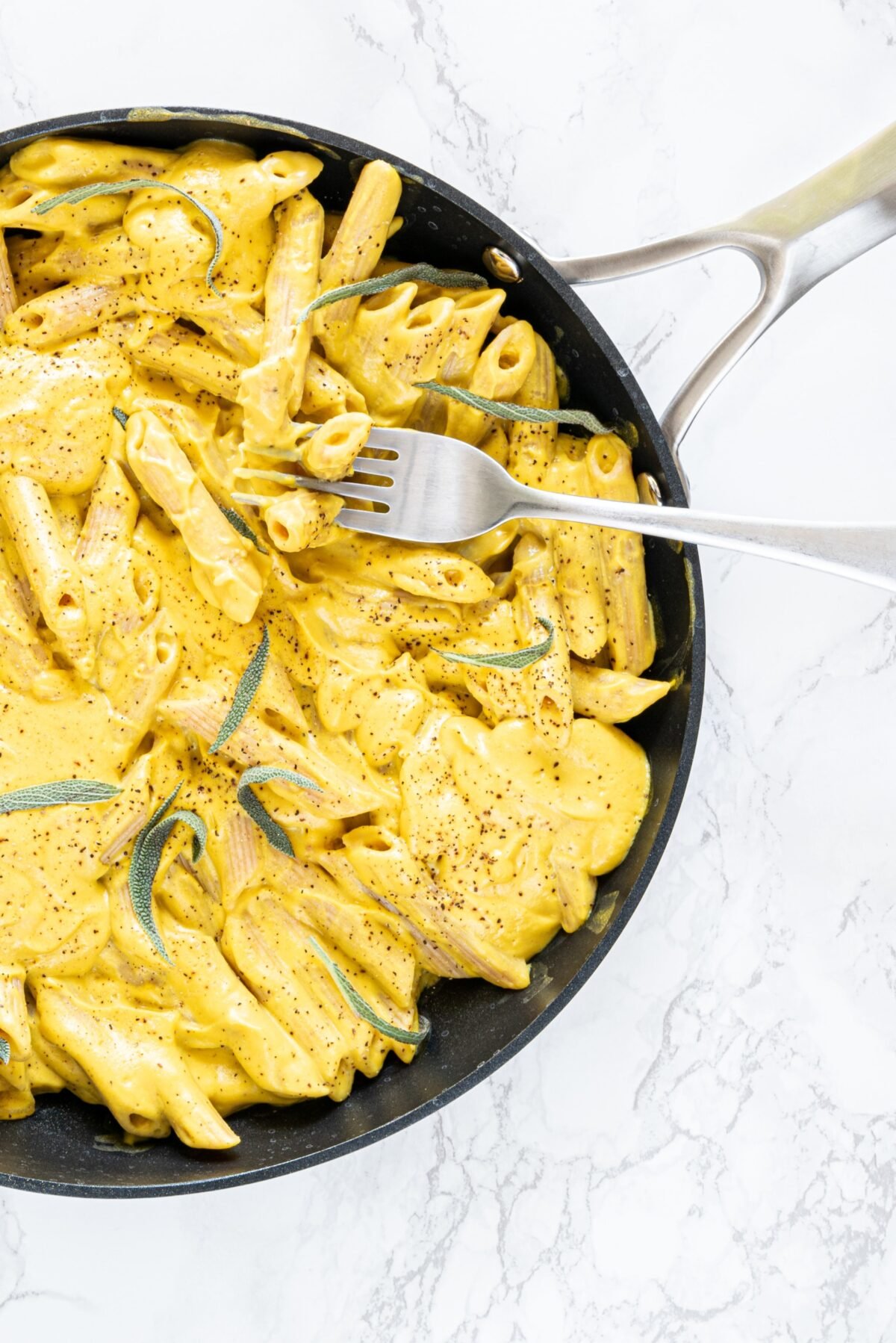 A pan filled with penne pasta with a cream sauce on it and a silver fork sticking out.
