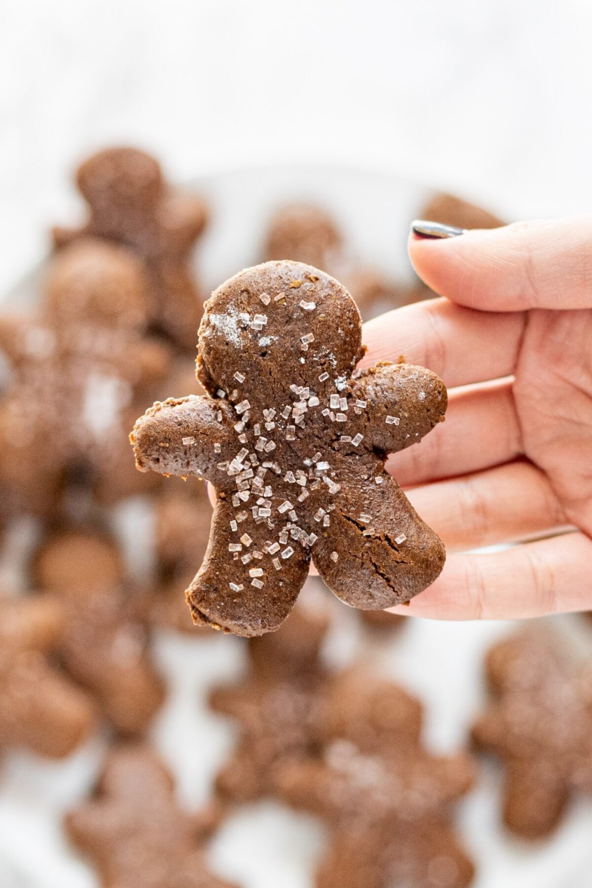 A white hand holding a gingerbread man cookie over a plate of remaining gingerbread cookies.
