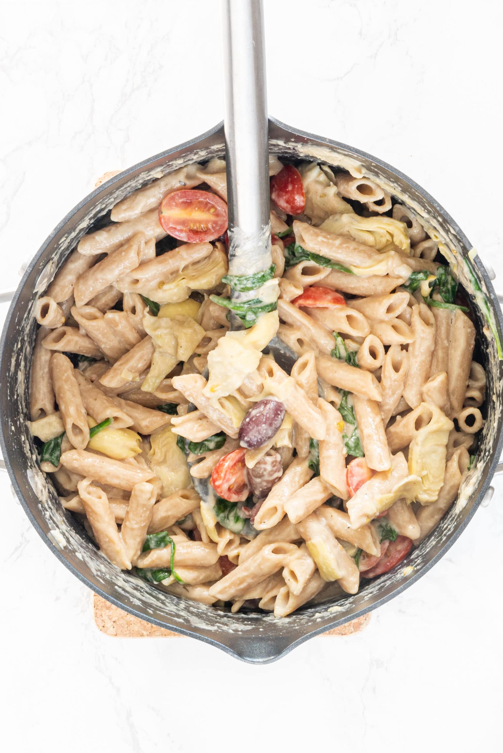 A silver pot filled with creamy vegan hummus pasta with a spoon sticking out of the pot.