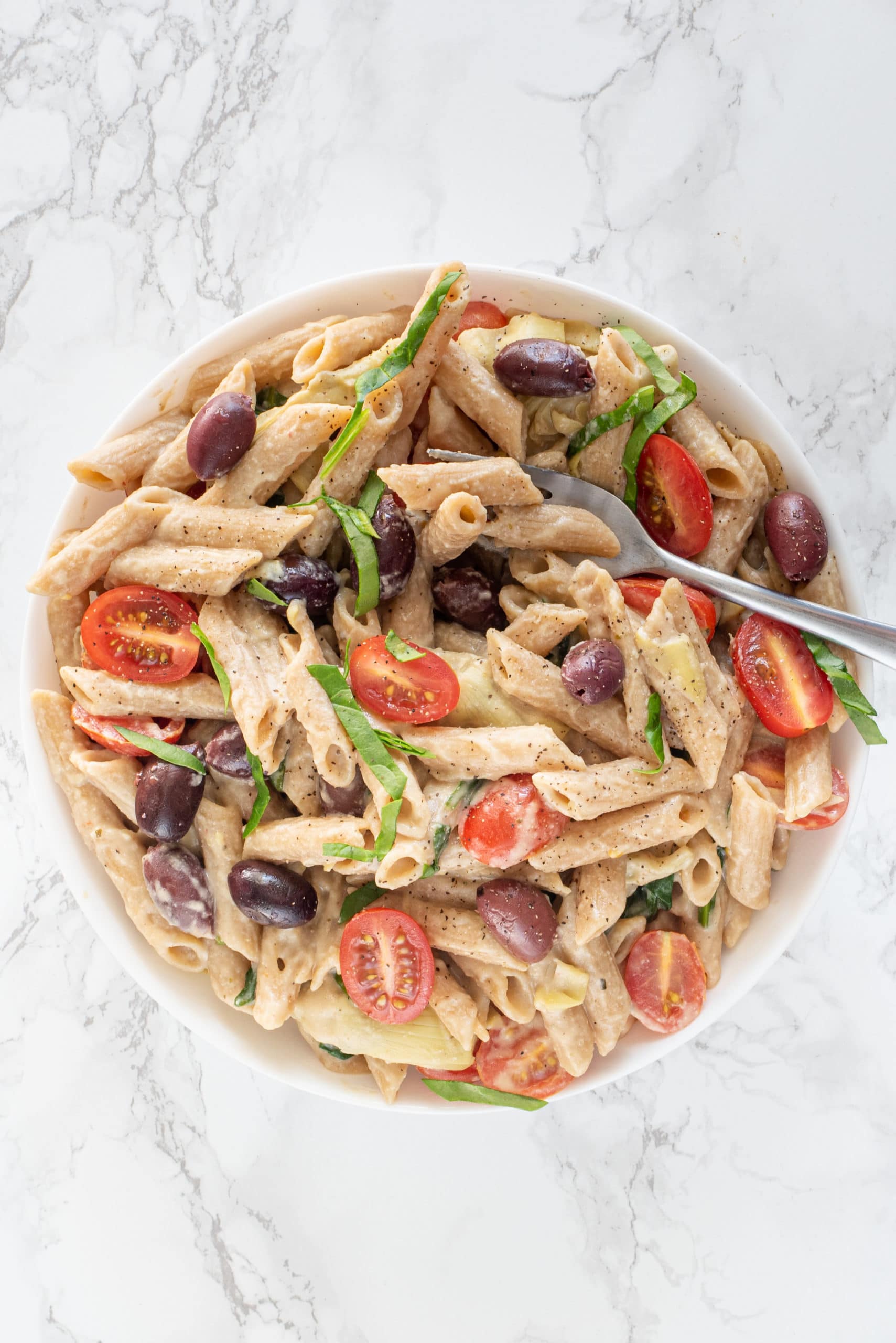 A white bowl filled with creamy vegan hummus pasta with a small fork in it.