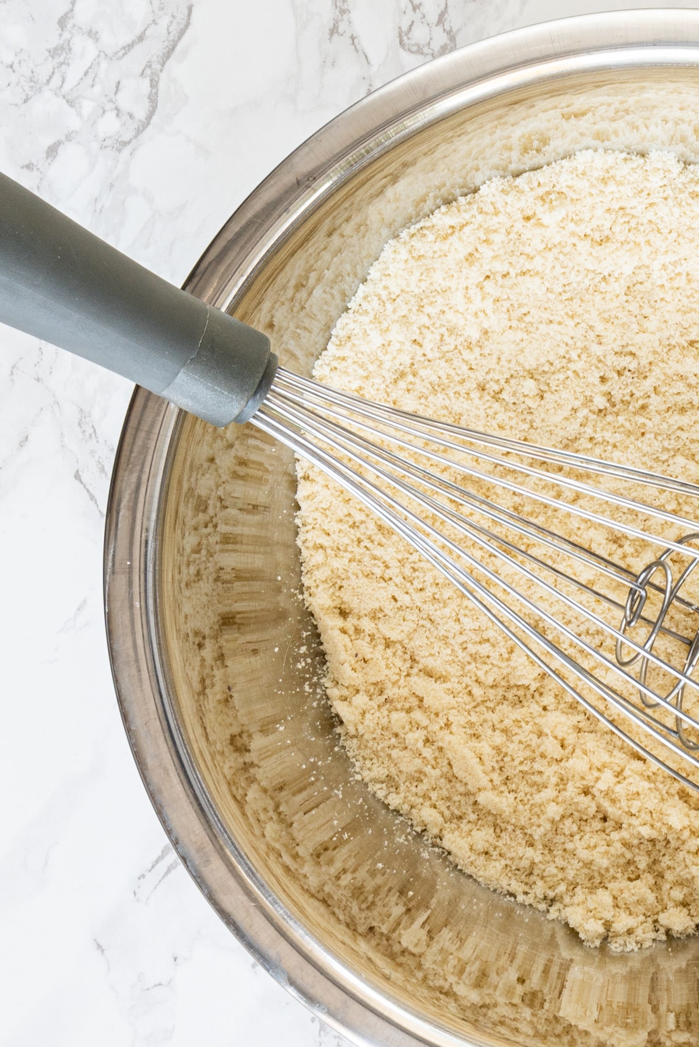 A silver bowl of almond flour and a whisk.