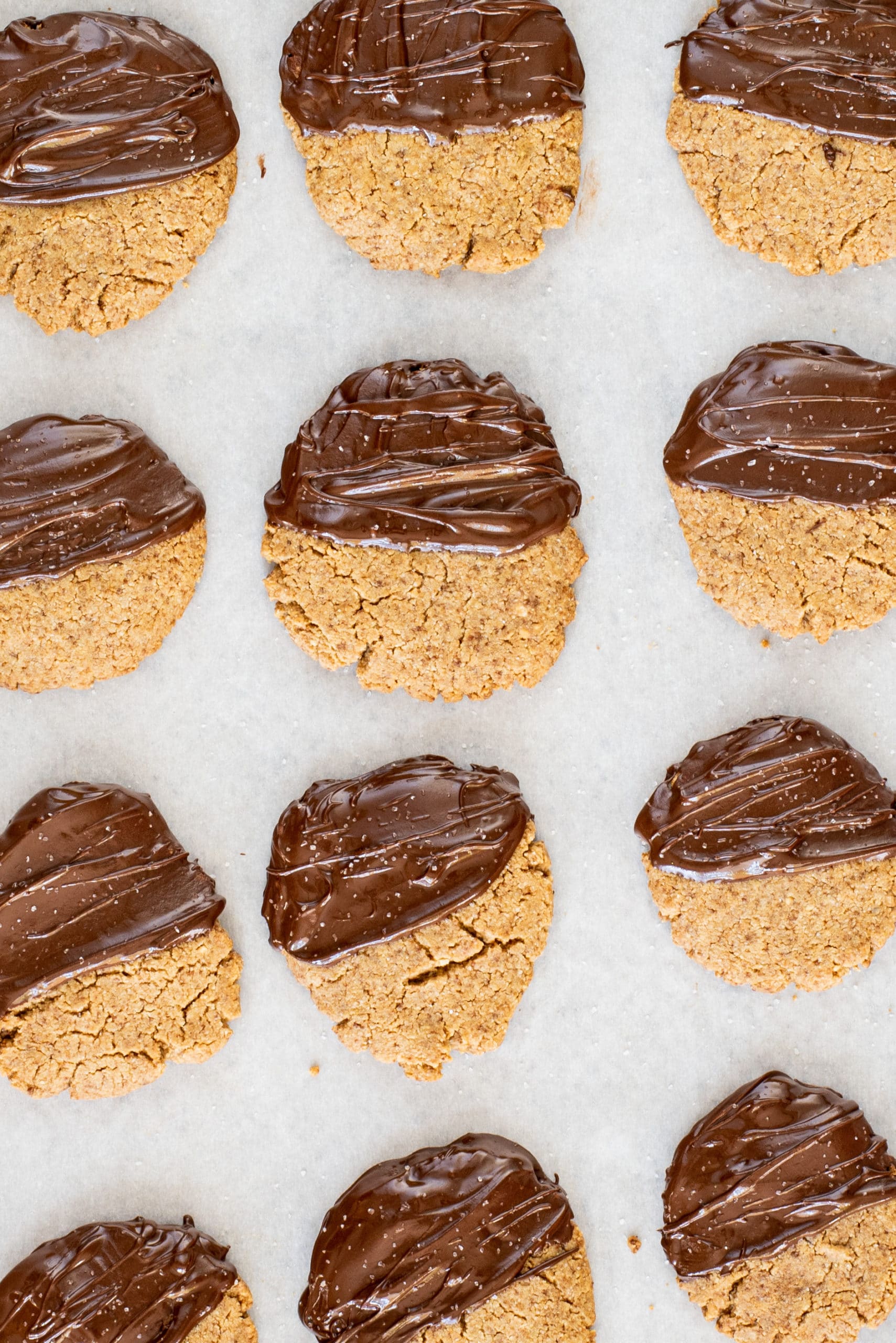 A pan lined with parchment paper and peanut butter cookies dipped in chocolate.