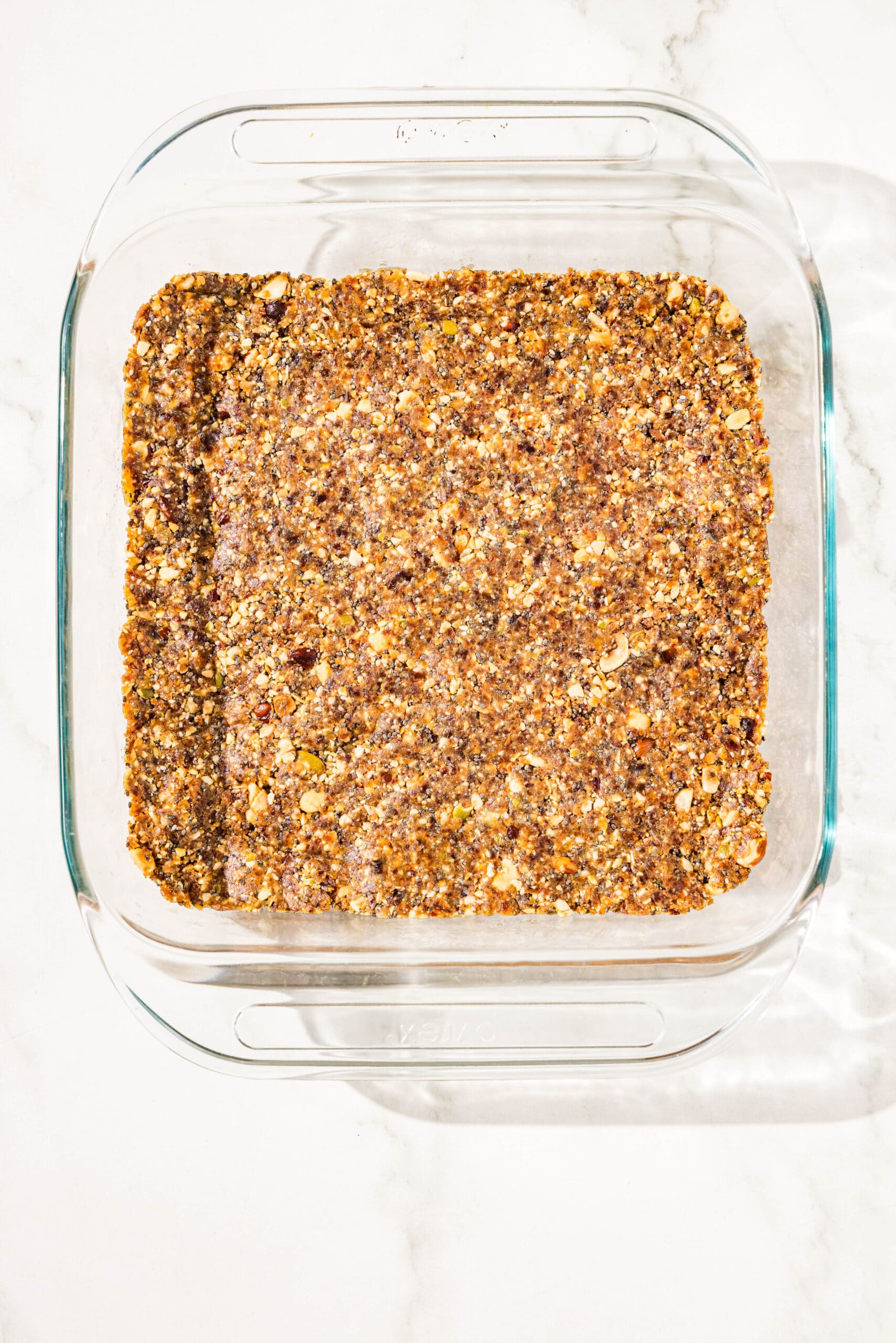 A clear 9x9 glass baking pan with a layer of homemade vegan protein bars pressed into the bottom.