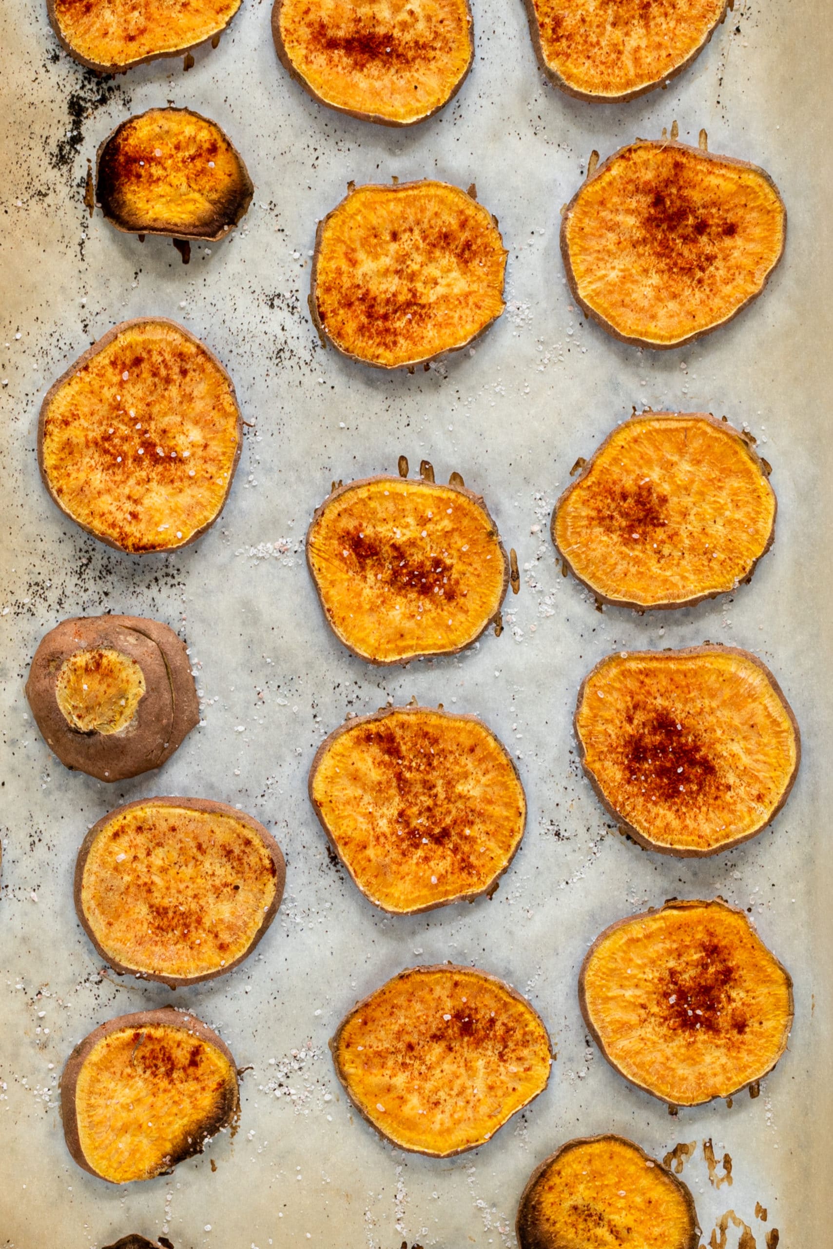 A parchment lined pan with slices of sweet potato on it.