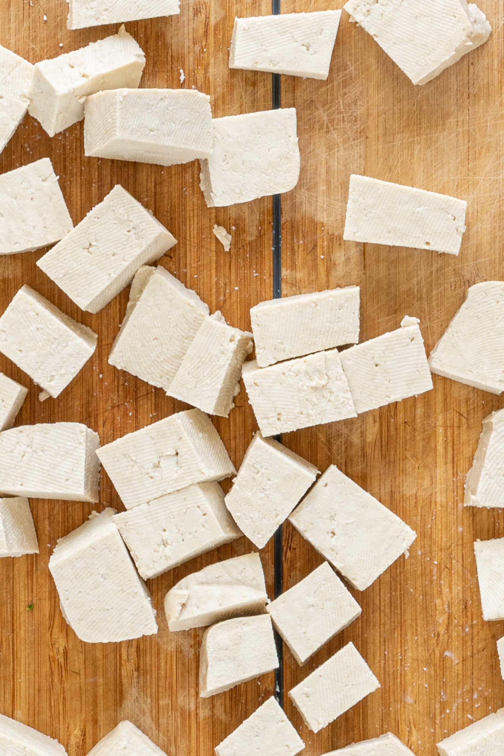 A brown cutting board with cubes of raw tofu on it.