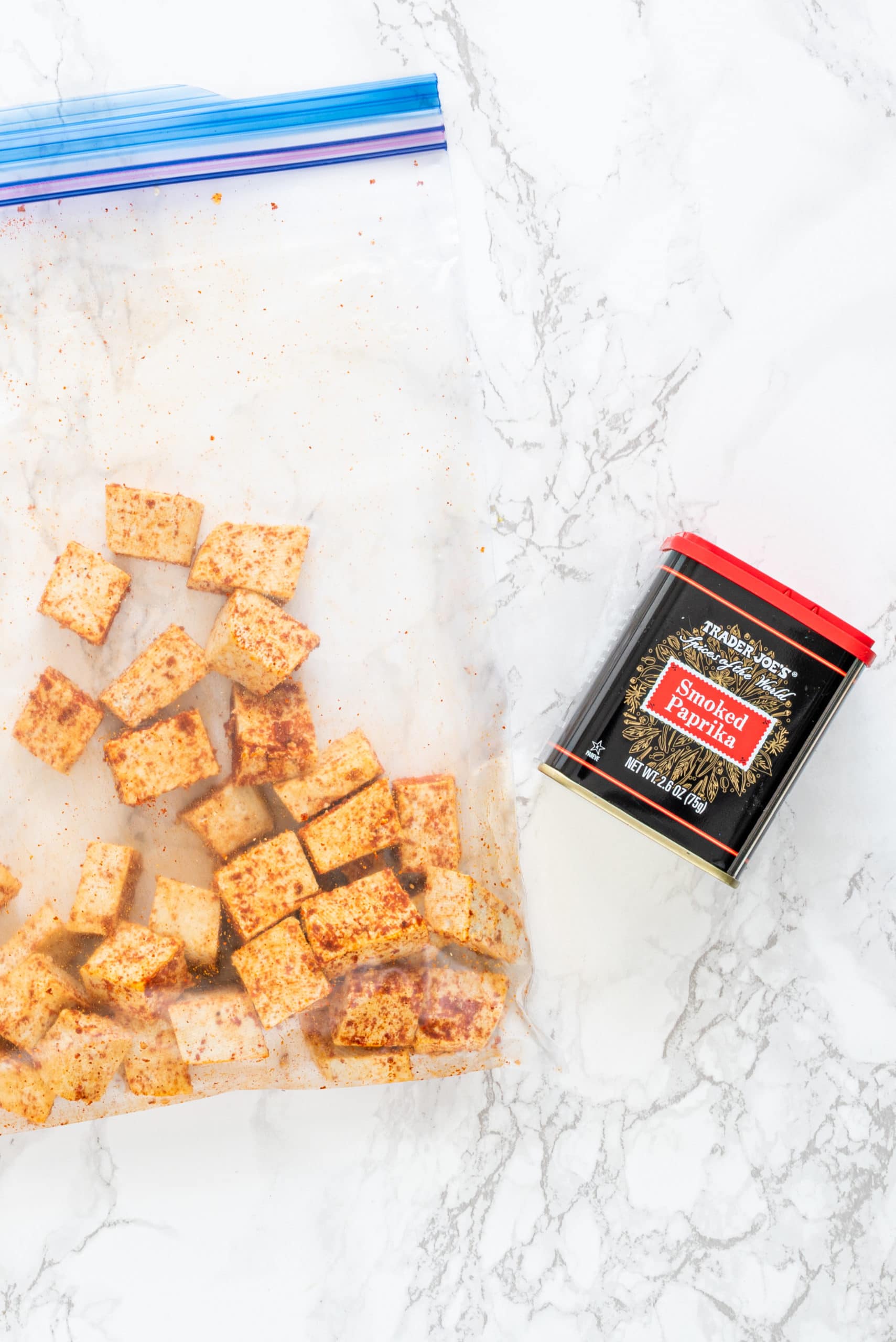 A clear plastic baggie filled with tofu cubes shaken in spices and a red and black container of smoked paprika.