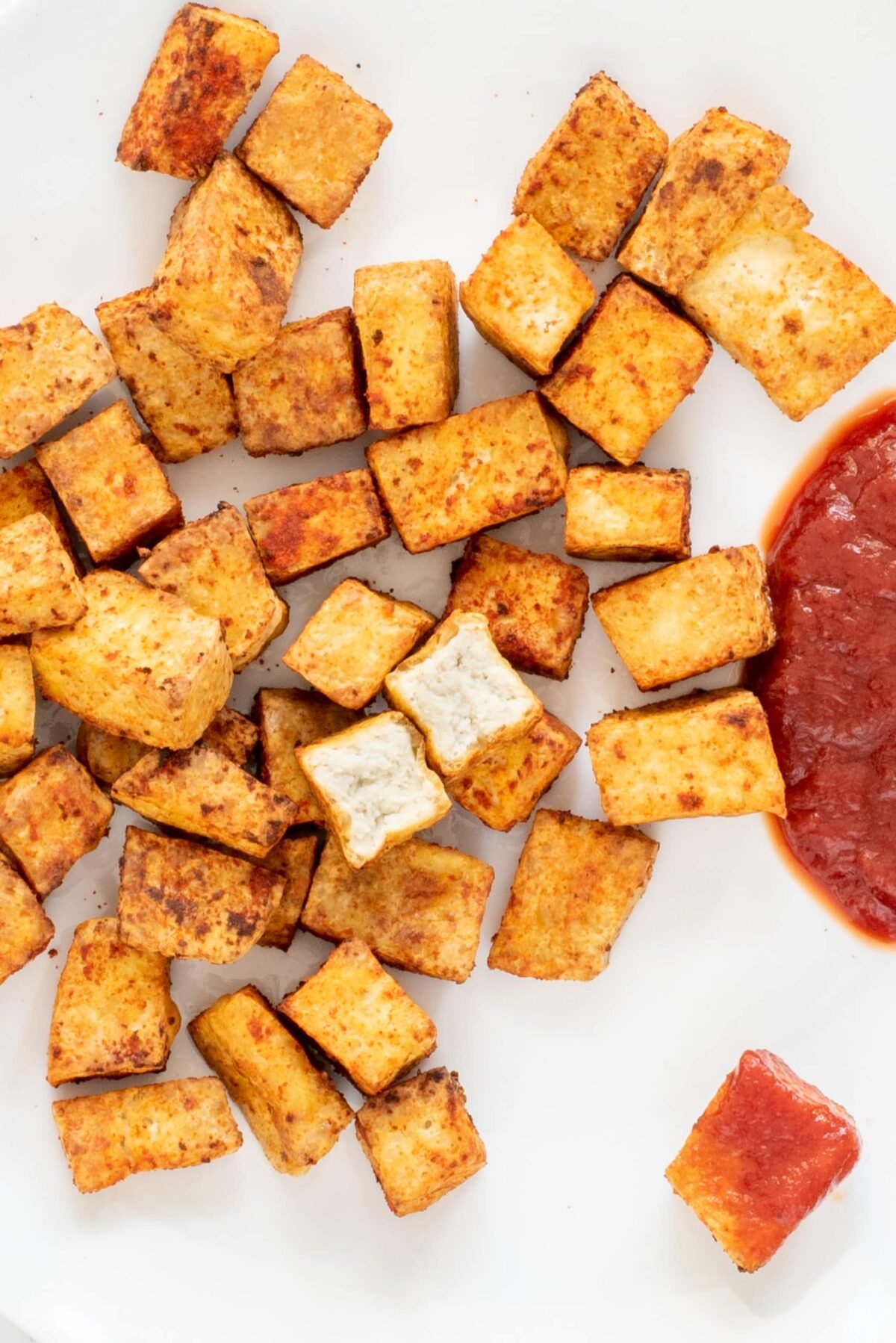 A white plate of vegan air fried tofu nuggets and some ketchup.