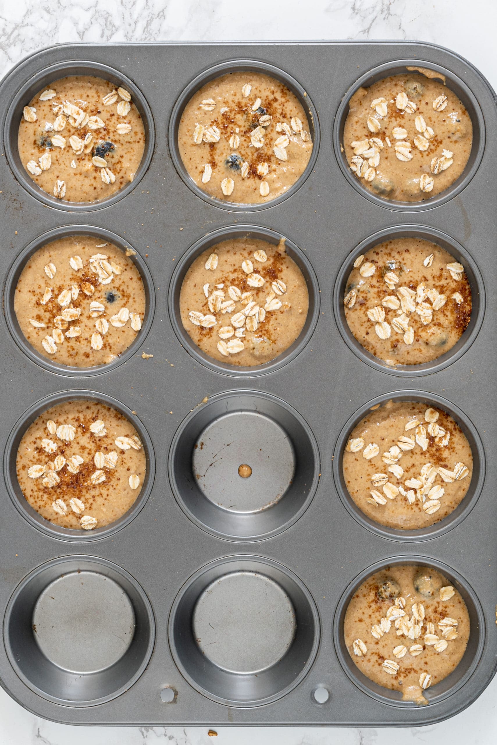 A silver muffin tin filled with blueberry muffin batter in 9 of the muffin compartments.
