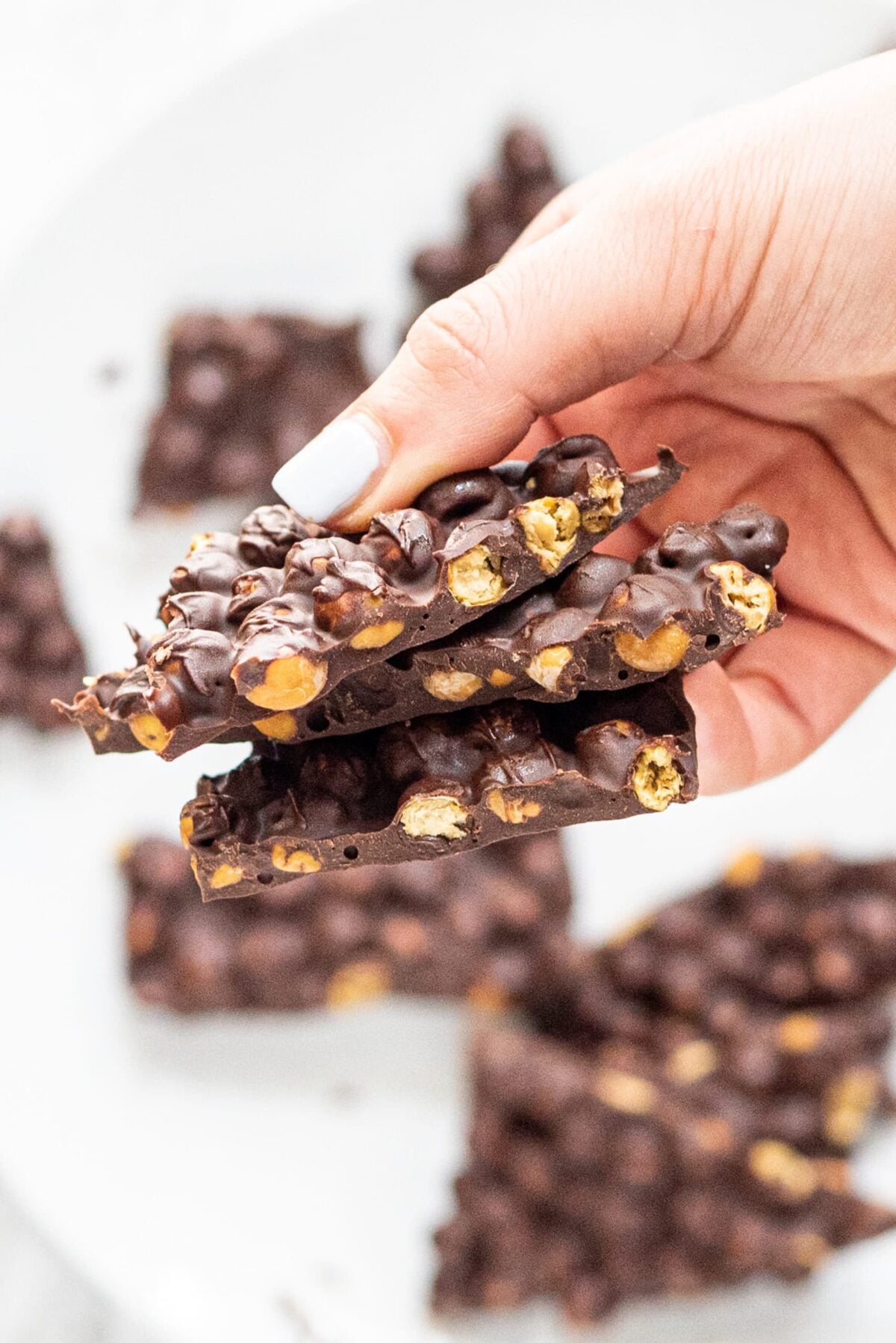 A white hand holding a stack of chocolate chickpea bark.