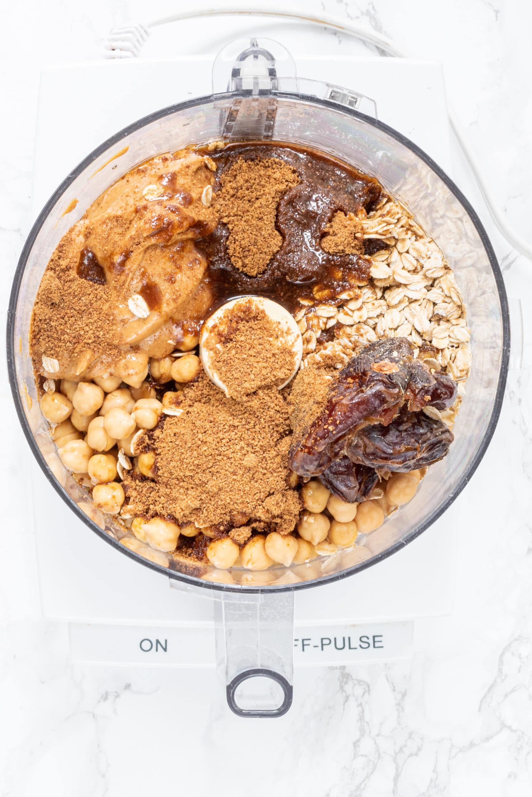 A food processor filled with chickpeas, peanut butter, medjool dates, oats, and cinnamon.