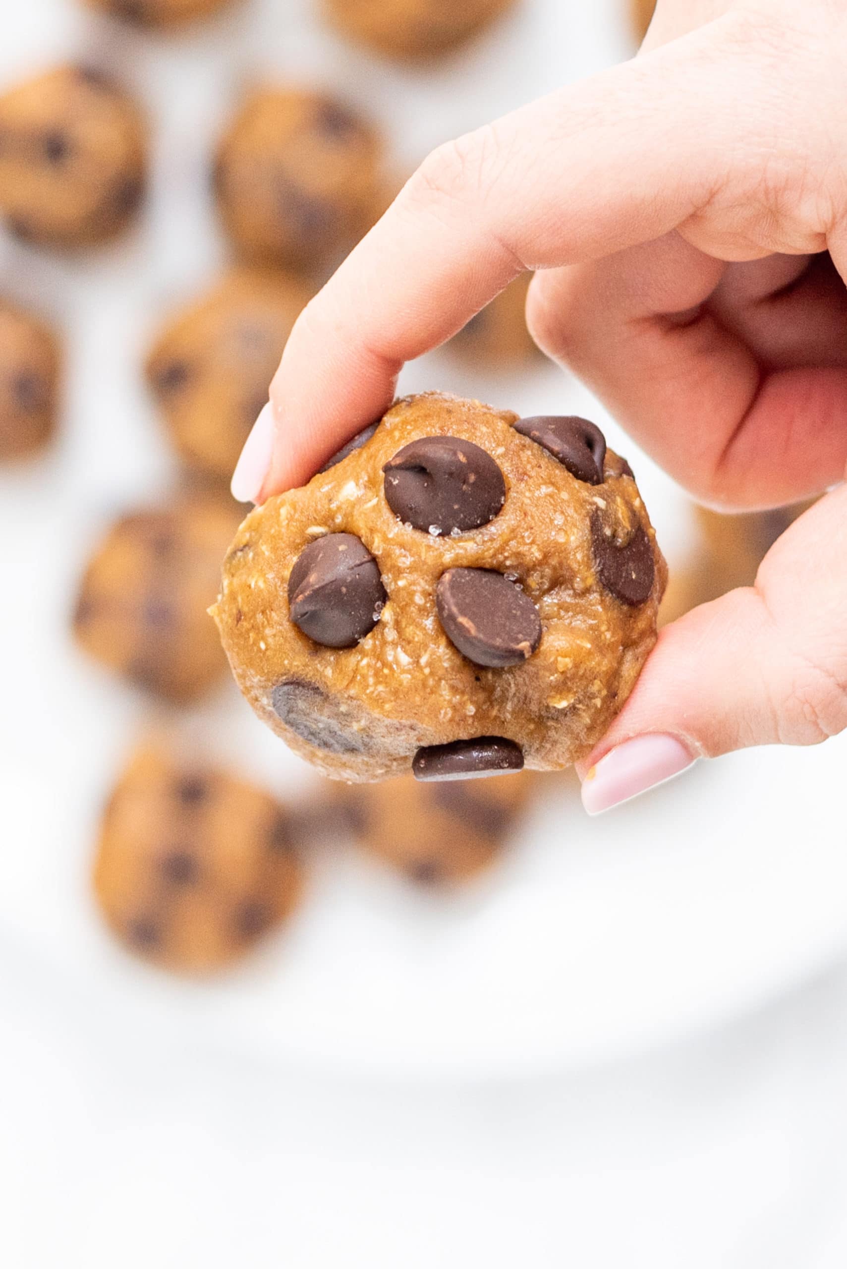 A white hand holding a chocolate chip cookie dough bite.