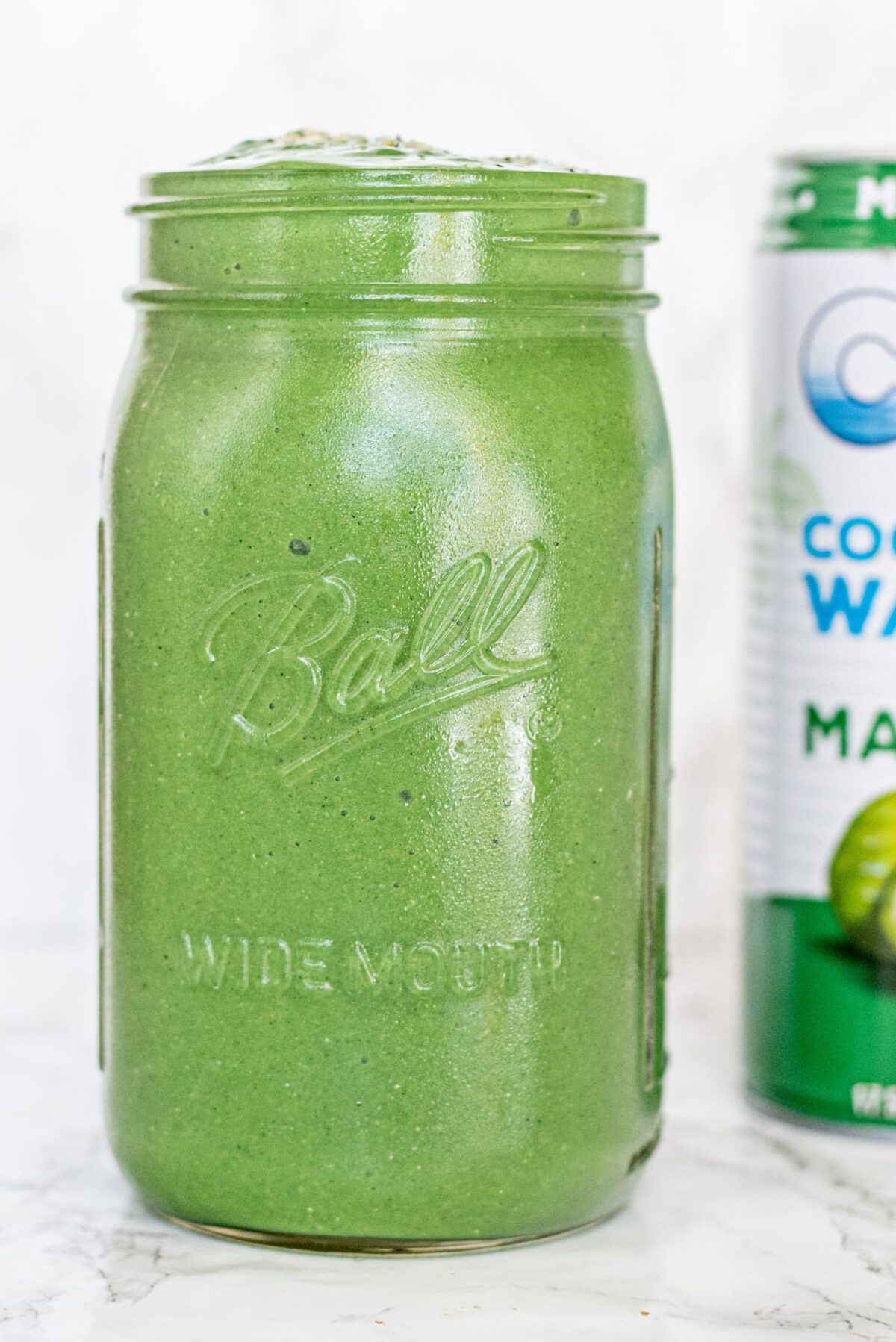 A green smoothie in a glass jar and a bottle of coconut water.