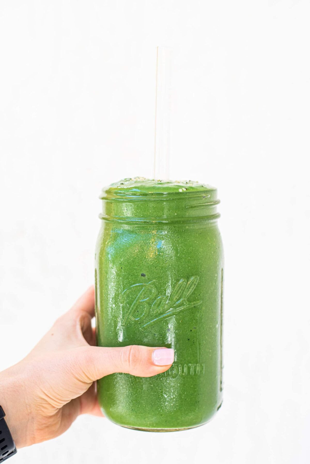 A white hand holding a tall mason jar green smoothie.