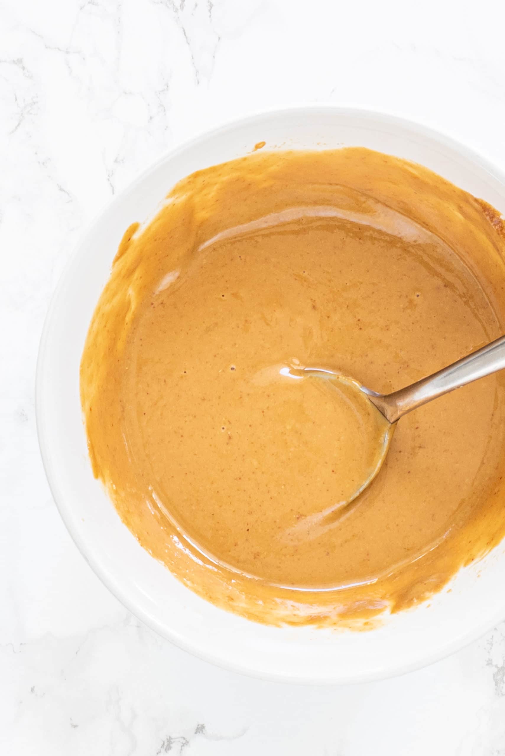 A white bowl filled with creamy peanut sauce.