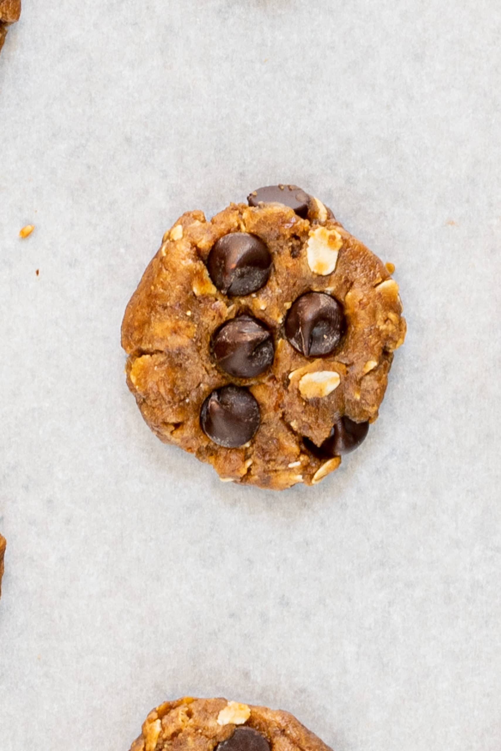 A chocolate chip cookie unbaked on a parchment paper lined baking sheet.
